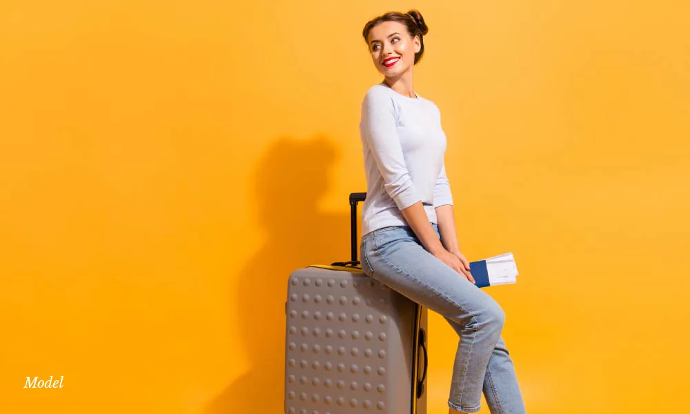 Young woman sitting on a Luggage on yellow background